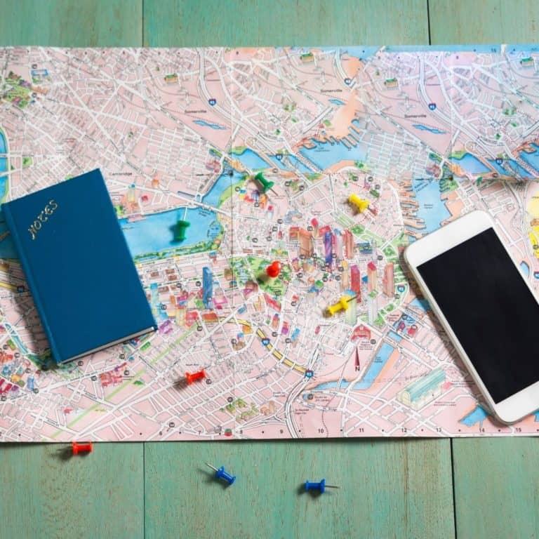 Map with pins on it along with a phone a blue notebook on the map