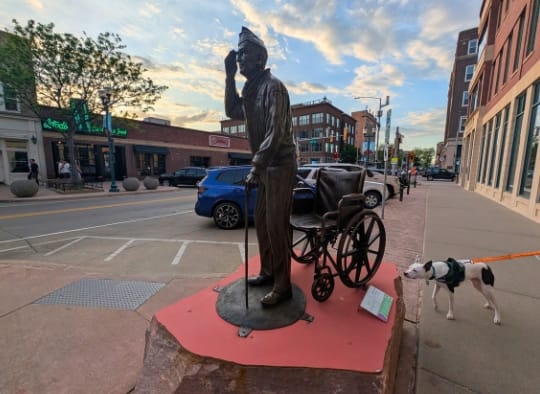 Black and white dog sniffing a Veteran sculpture at Sculpture Walk Sioux Falls