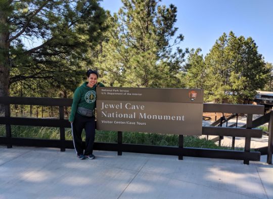 Woman standing next to Jewel Cave National Monument Sign