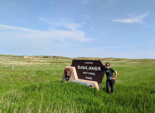 woman next to sign that says Leaving Badlands National Park