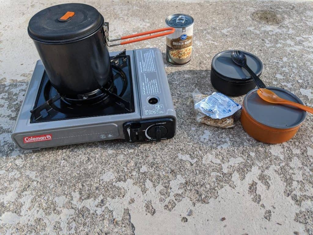 Camping stove with a pot on top of it and two bowls and sporks nearby
