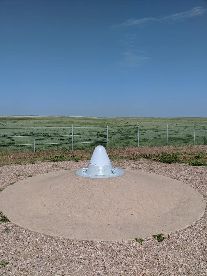 Another part of Delta-09 Missile Silo. There is a white coned cap above ground in the center of a mound of pavement.  