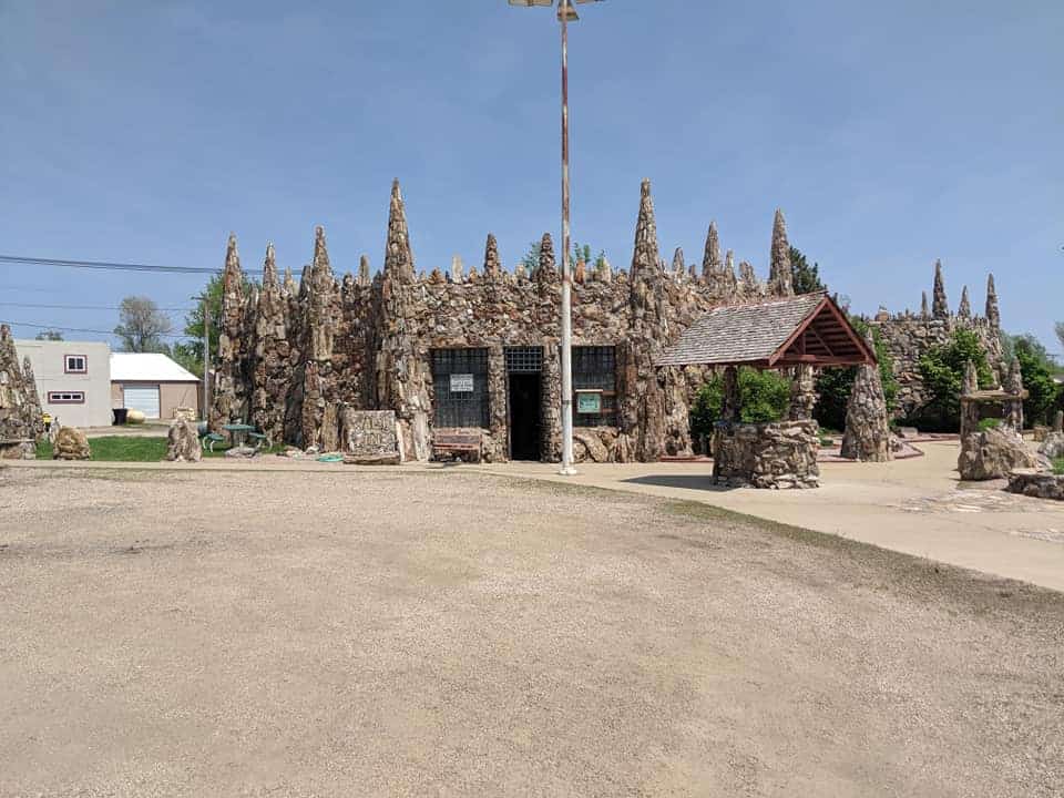 The Petrified Wood Park Museum Building made of petrified wood. There is a main door opening and a window on each side of the door. There is a well also made of petrified wood in front of the building.