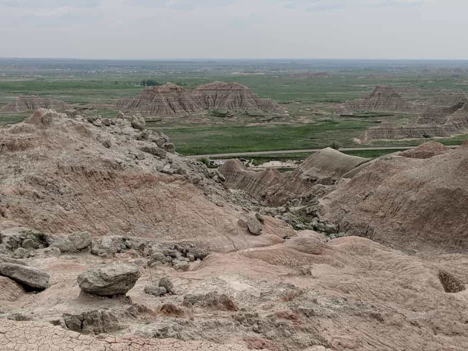 Looking out into Badlands National Park from the top of Saddle Pass Trail. There are several hills made of rock in the distance in the middle of grass fields.