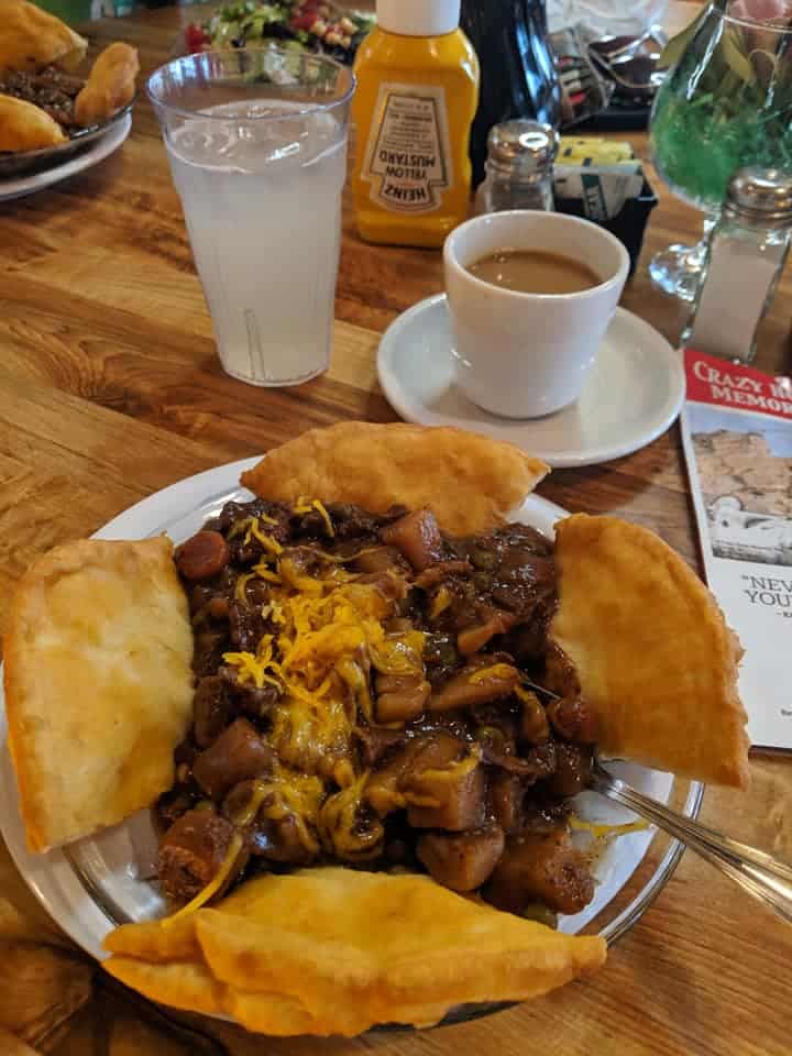 Plate of Tatanka (Bison) stew in the middle of a white bowl. There are 4 pieces of fry bread spaced around  the outer edges of a bowl.