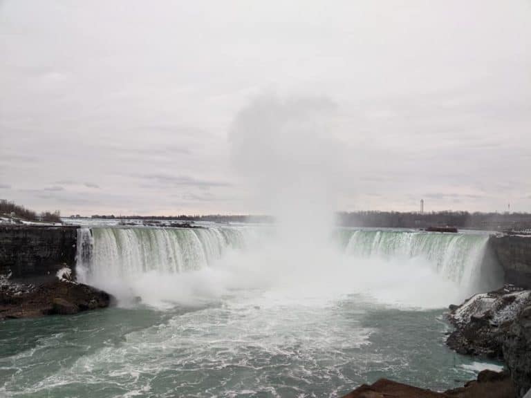 Photo of the Horseshoe Falls part of Niagara Falls in winter. There is snow and ice on the land around the falls