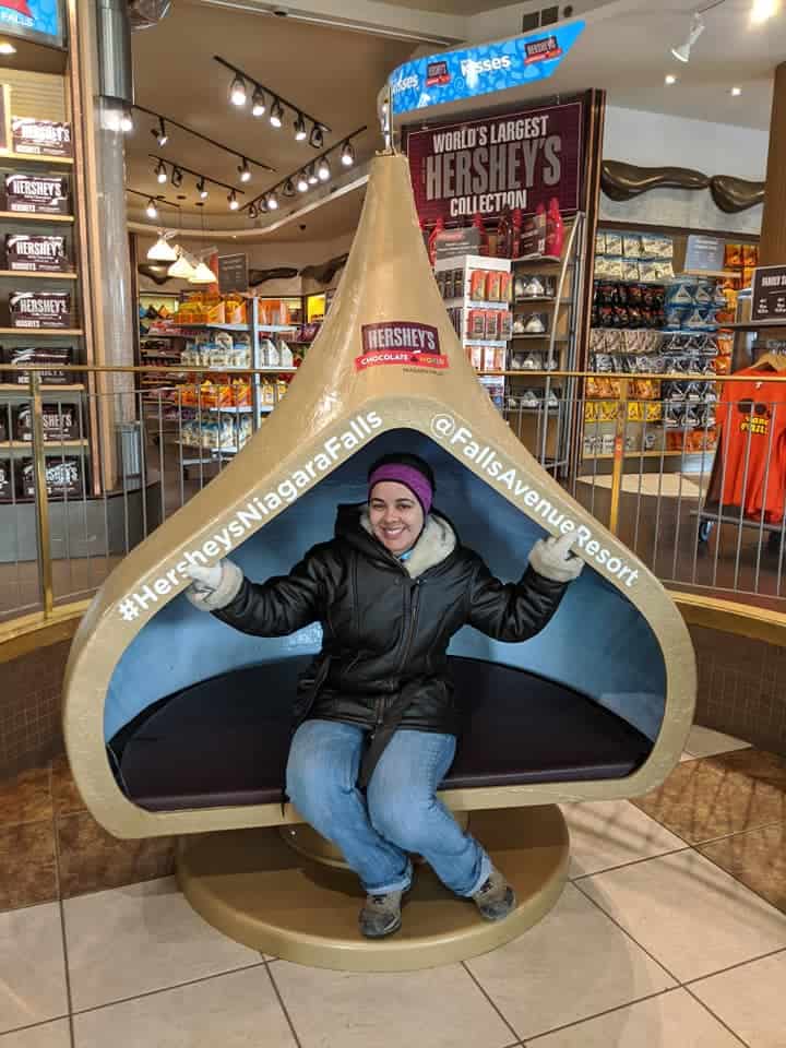 Woman in a heavy leather jacket sitting inside a bench in the shape of a hollowed out Hershey kiss.