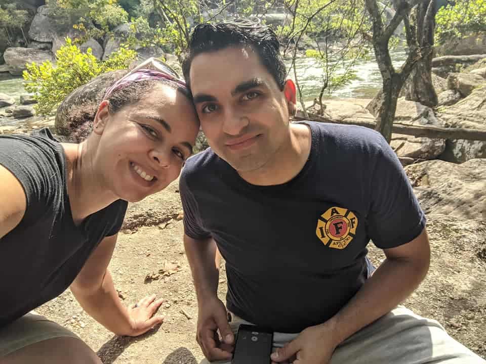 Woman leaning towards a man, both smiling at camera. There is a river in Cumberland State Park in the background.