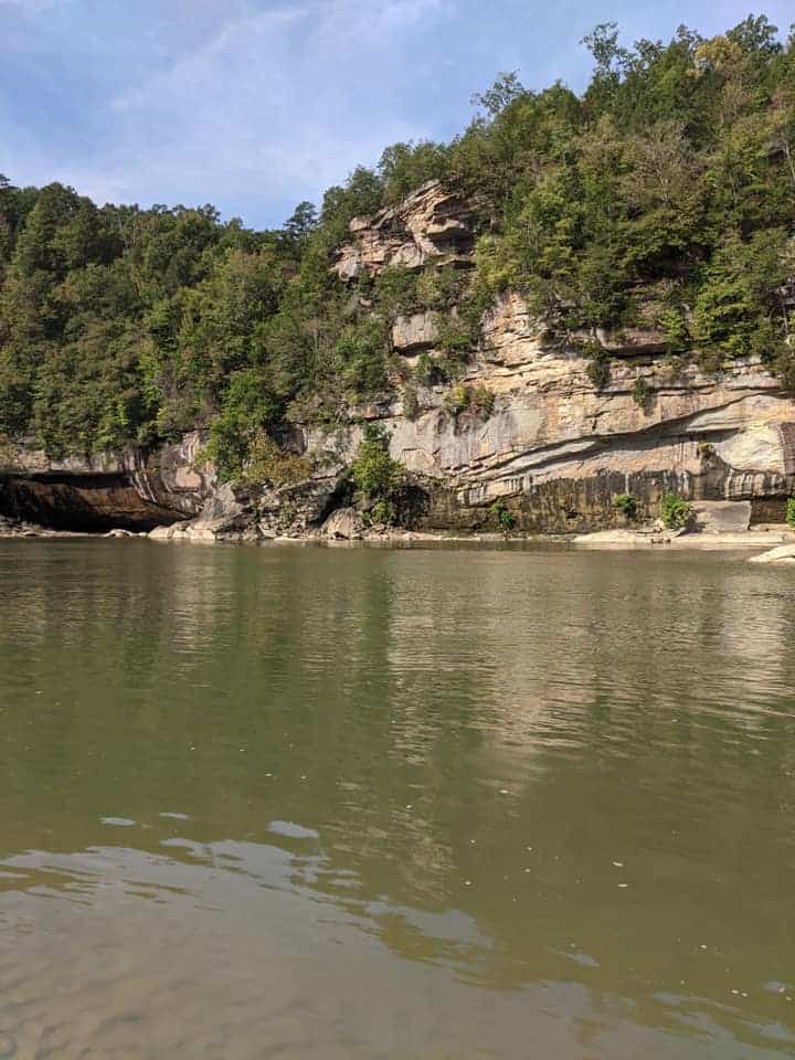 View looking out across the river in Cumberland State Park. Across the river is a tall wall of rock with trees growing around and from it.