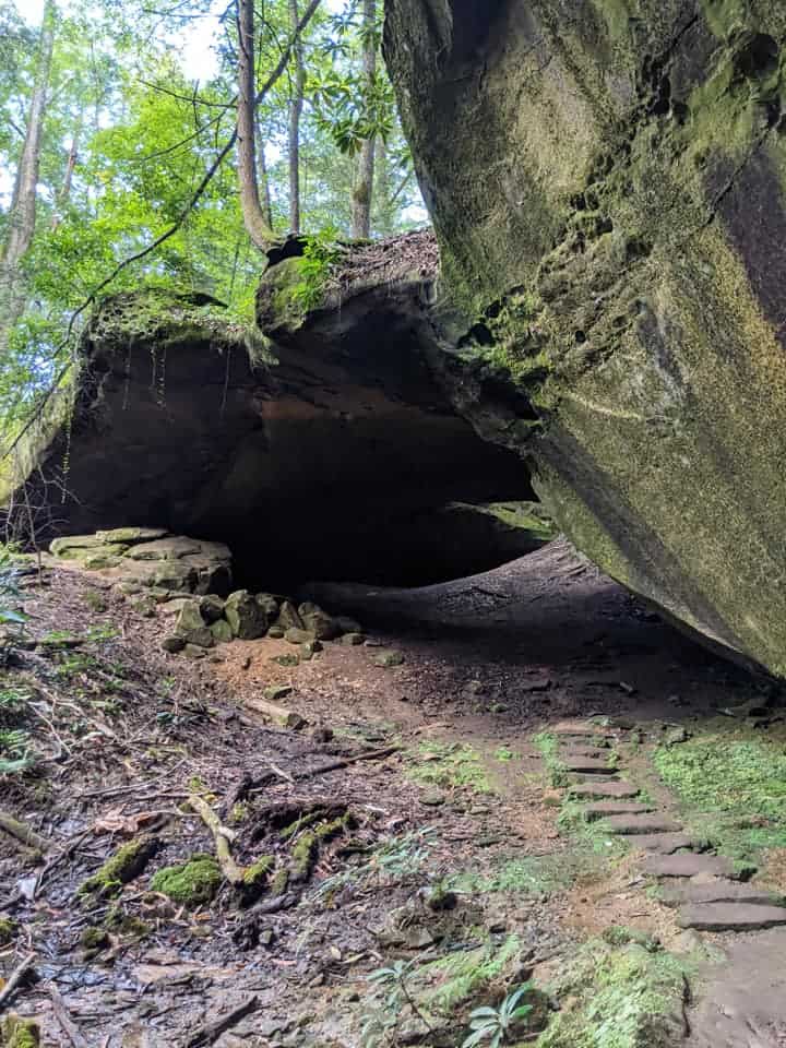 View approaching Yahoo Arch. There is some small stone steps leading up to it with some bright green trees behind the arch.