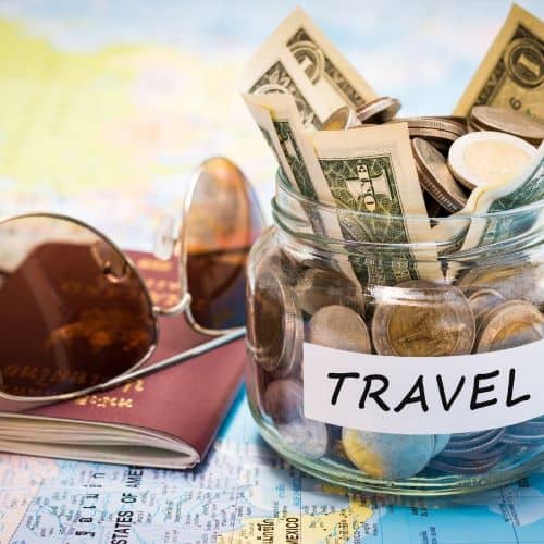 Jar of money that says travel on it. Next to it are sunglasses on top of a passport.  All of these items are on top of a map