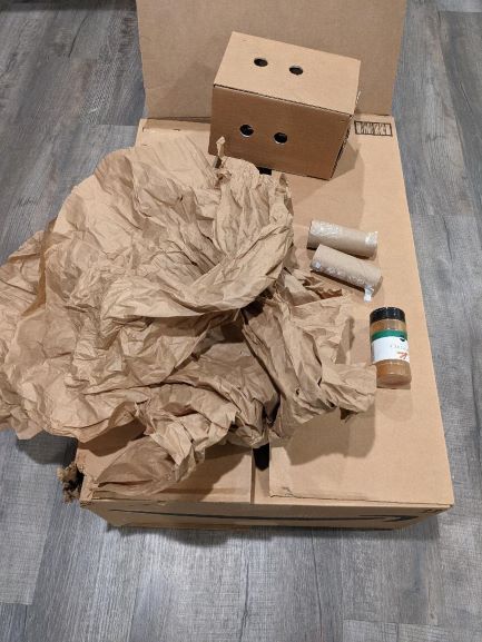 2 cardboard boxes, 2 empty cardboard toilet paper rolls, a container of cinnamon, and several pieces of brown packing paper