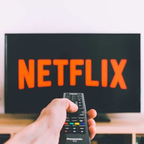 Person holding a remote pointed at a tv that says Netflix