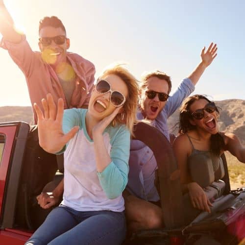 Group of people having fun and posing for picture while hanging out the sides of their car