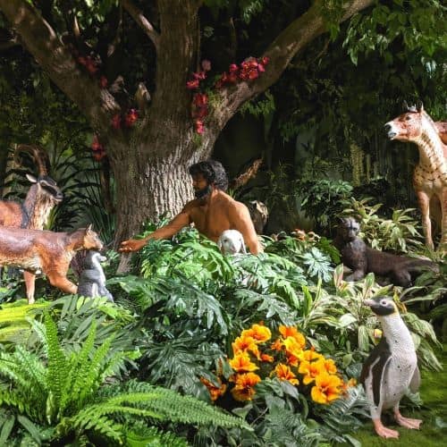 Display of Adam in the Garden of Eden surrounded by all types of animals like penguins and large cats.