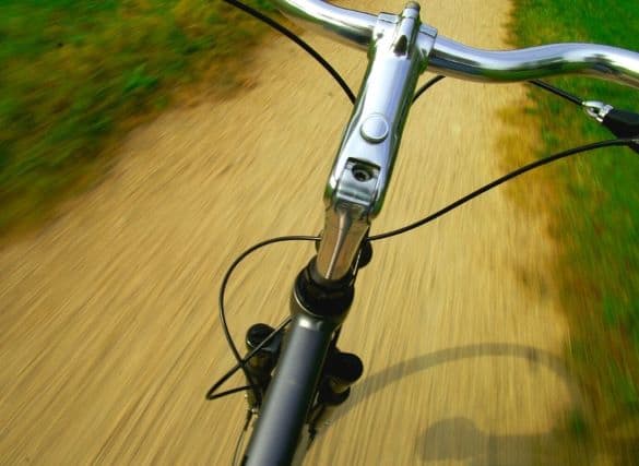 View of a bike handle from above while it is moving down a gravel path