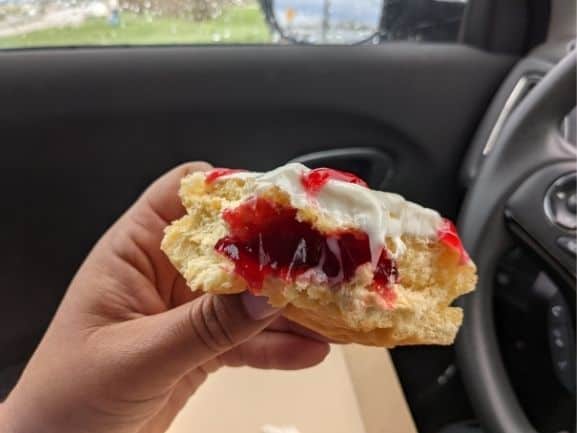 Half of a cherry-filled donut with white cheese cake frosting. You can see the cherry filling in the middle.