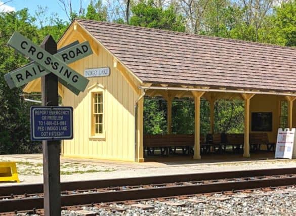 The Indigo Lake Scenic Railway Station in Cuyahoga Valley National Park. The station is yellow with benches inside. There is a train track and Railroad crossing sign in the foreground.