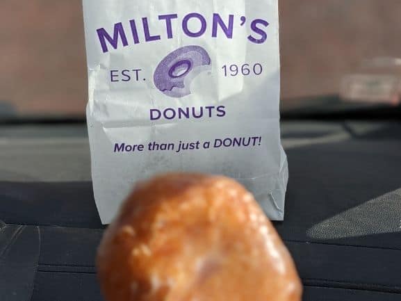 A deep fried cream cheese donut in font of a white Milton's donuts bag