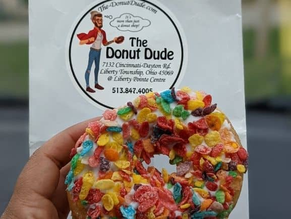 Fruity pebble donut, covered with fruity pebbles in front of a The donut dude bag