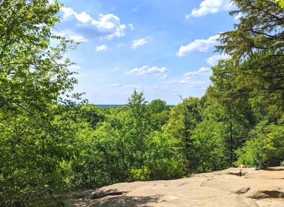 The Ledges Scenic Overlook. The sky is blue with several white clouds. There is a rock ledge that looks out over a forest.