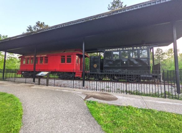2 train cars. One is black and the other is red. Both Say Mammoth cave R.R. Co. written in white near the roof of both cars.