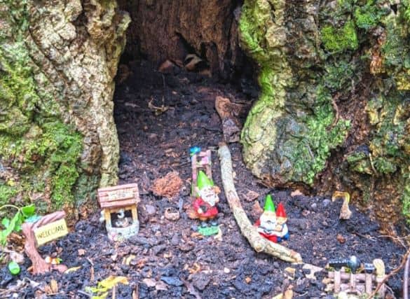 A small gnome village at the base of a hollowed out tree. there is a welcome sign, well, and three gnomes.