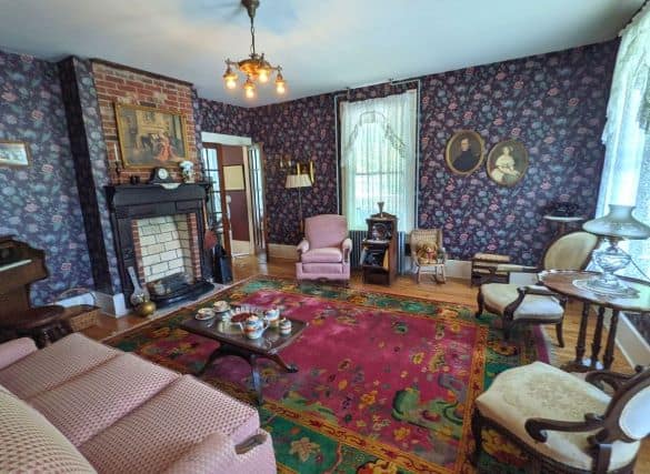 Room inside the Superintendent's house. It is a living room with a couch and several chairs, a piano, fake fireplace and paintings on the wall