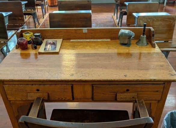View of a one room school house from the teacher's desk. You can se several rows of old-fashioned wooden desks for students 