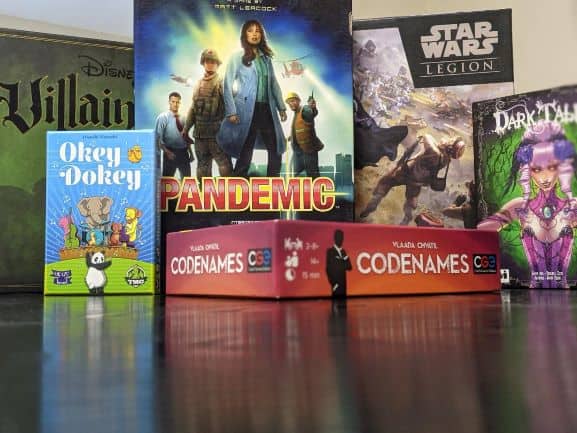 6 board games displayed on a table; Disney Villainous, Pandemic, Okey Dokey, Code Names, Star Wars Legion, and Dark Tales