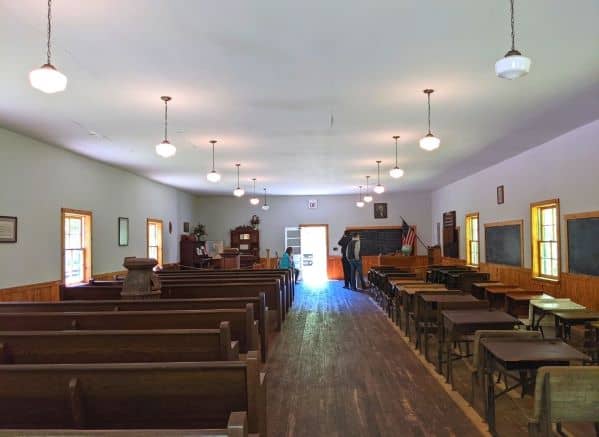The inside of the church/school building for the Barthell Coal Camp. The left side is full of pews and the right side is full of school desks.