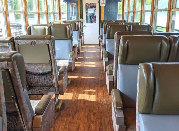 View down the aisle inside one of the train passenger cars. Floor looks like wood and there are two brown seats on both sides of the aisle