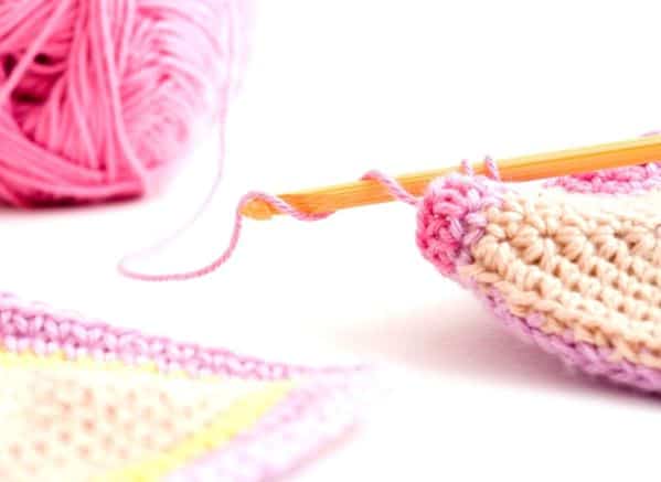 A ball of pink yarn attached to a crochet needle. There are 2 pieces of crocheted pieces displayed.