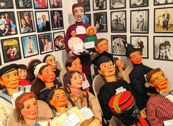 Man with his back to the camera looking at a wall of ventriloquist dummies and photos