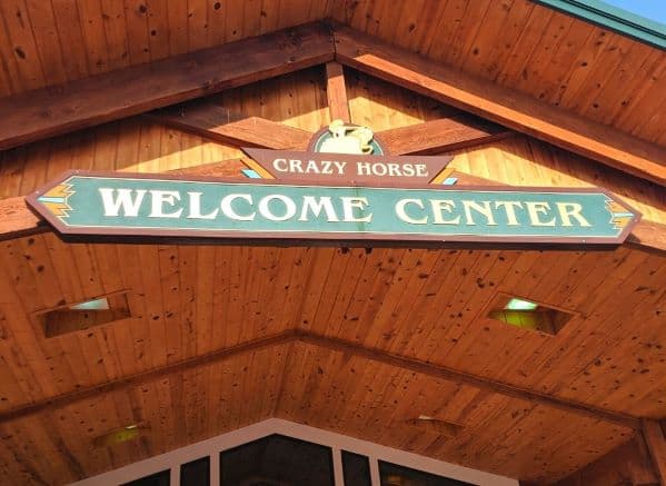 The "Crazy Horse Welcome Center" sign on the front of the wooden building.