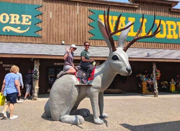 Two women sitting and smiling on the large plastic Jack O' Lope sculpture in front of Wall Drug