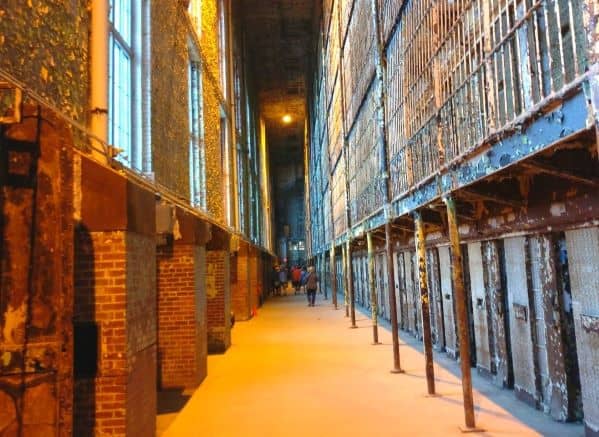 View down a corridor at the Ohio State Reformatory. There is a brick wall with barred windows on the left and on the right are several levels of cell blocks