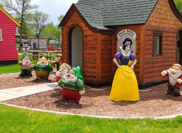 Statues of Snow White and the seven dwarfs posed in front of a wooden cottage in Storybook Island