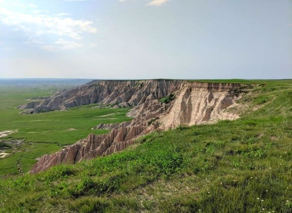 A landscape view inside Badlands National Park. It is of the edge of a mountain. The top of the mountain is flat and there is grass everywhere