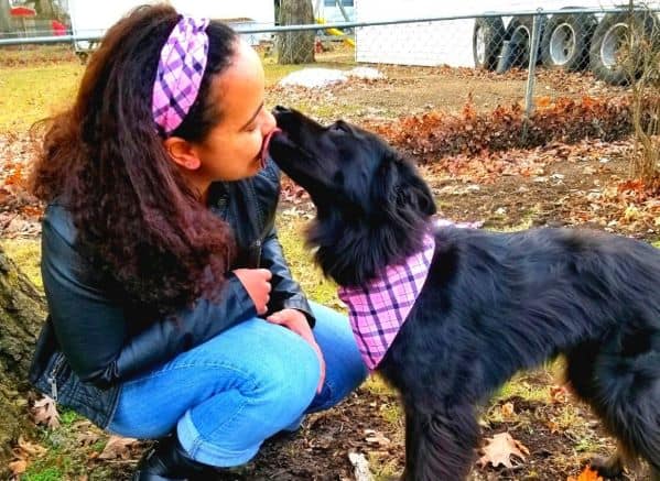 Black dog licking a woman's face. They are wearing matching pink checkered bandanas