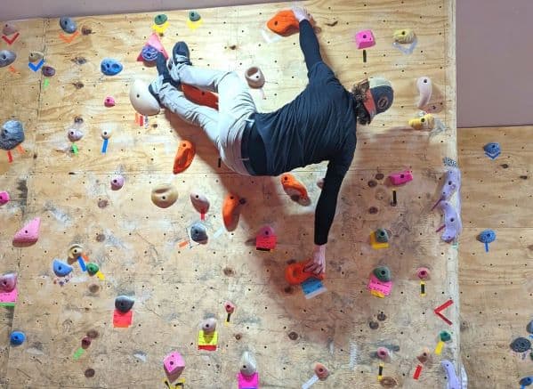 Man climbing a rock wall. His feet are in line with his top hand so he is parallel to the floor
