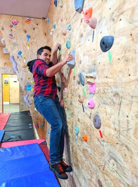 Man wearing plaid and jeans climbing on rock wall with a big smile on his face