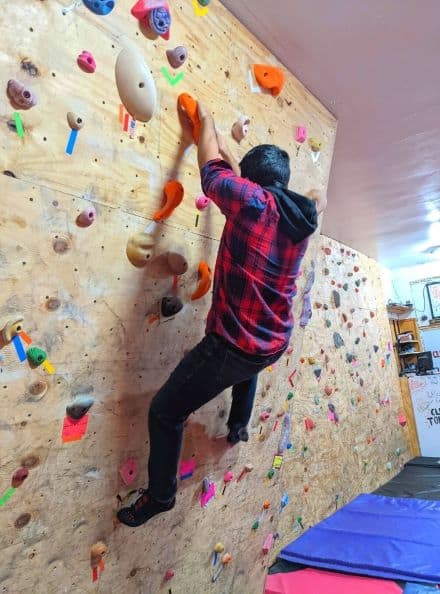 Man wearing plaid shirt climbing on bouldering wall in Climb Toledo