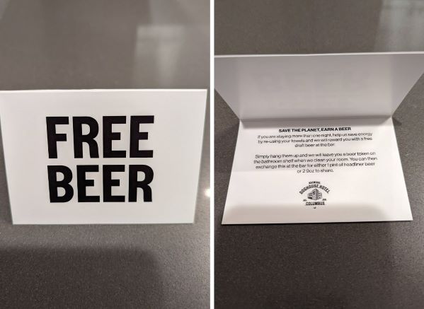 Free Beer card. States that you get a free beer for reusing your towels at DogHouse Hotel. Card is  A-frame shaped. Front of card has bold black text that reads, FREE BEER. Inside of card has instructions on how to receive FREE BEER TOKEN.