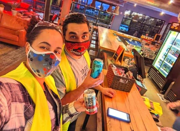 Man and woman wearing yellow vests holding beer in the DogHouse Hotel Lobby. 