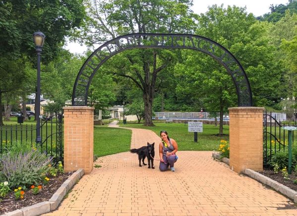 Woman kneeling next to her dog under an arch at the entrance to Berkeley Springs State Park