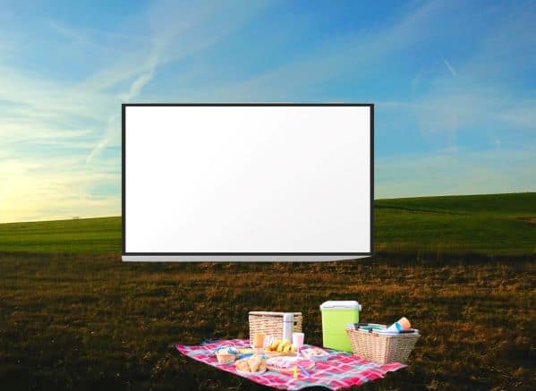 Movie screen in a field with a picnic set up on a blanket