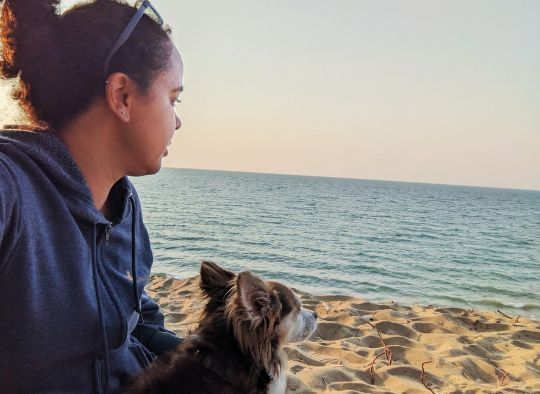 dog sitting in womans lap looking out over a body of water on a beach
