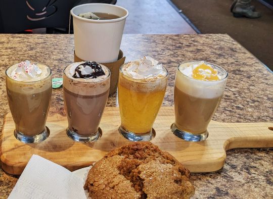 A sample tray of hot coffee beverages, a cup of tea, and a muffin