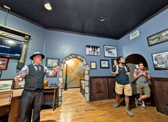 Tour Guide and two men with dogs in backpack in the New York Connection Gallery in Gangster Museum of America